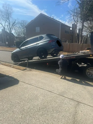 A gray SUV being loaded onto a flatbed tow truck on a residential street. A person is working.