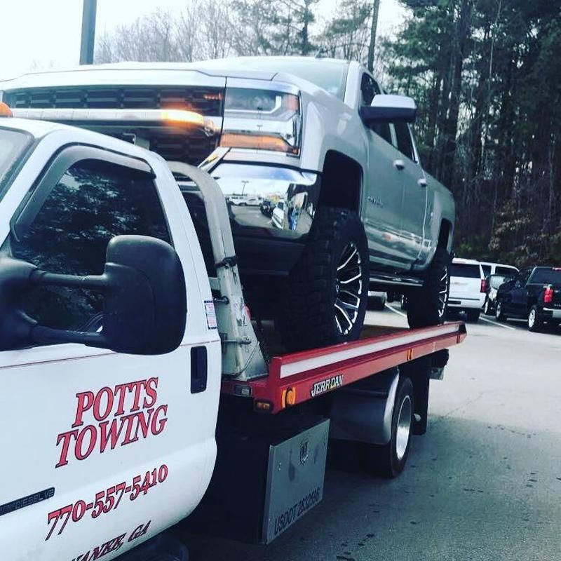 A silver truck is being towed by a potts towing truck