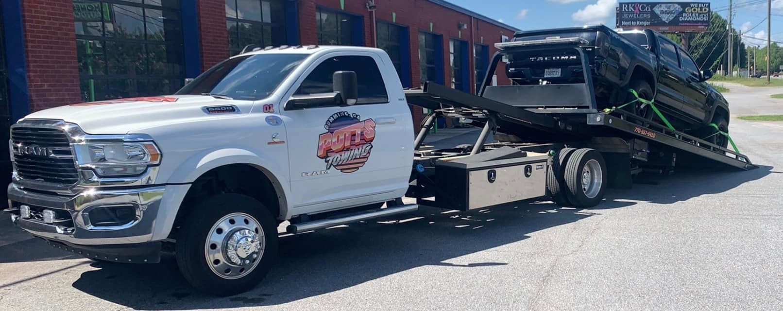 A white tow truck is towing a black car.