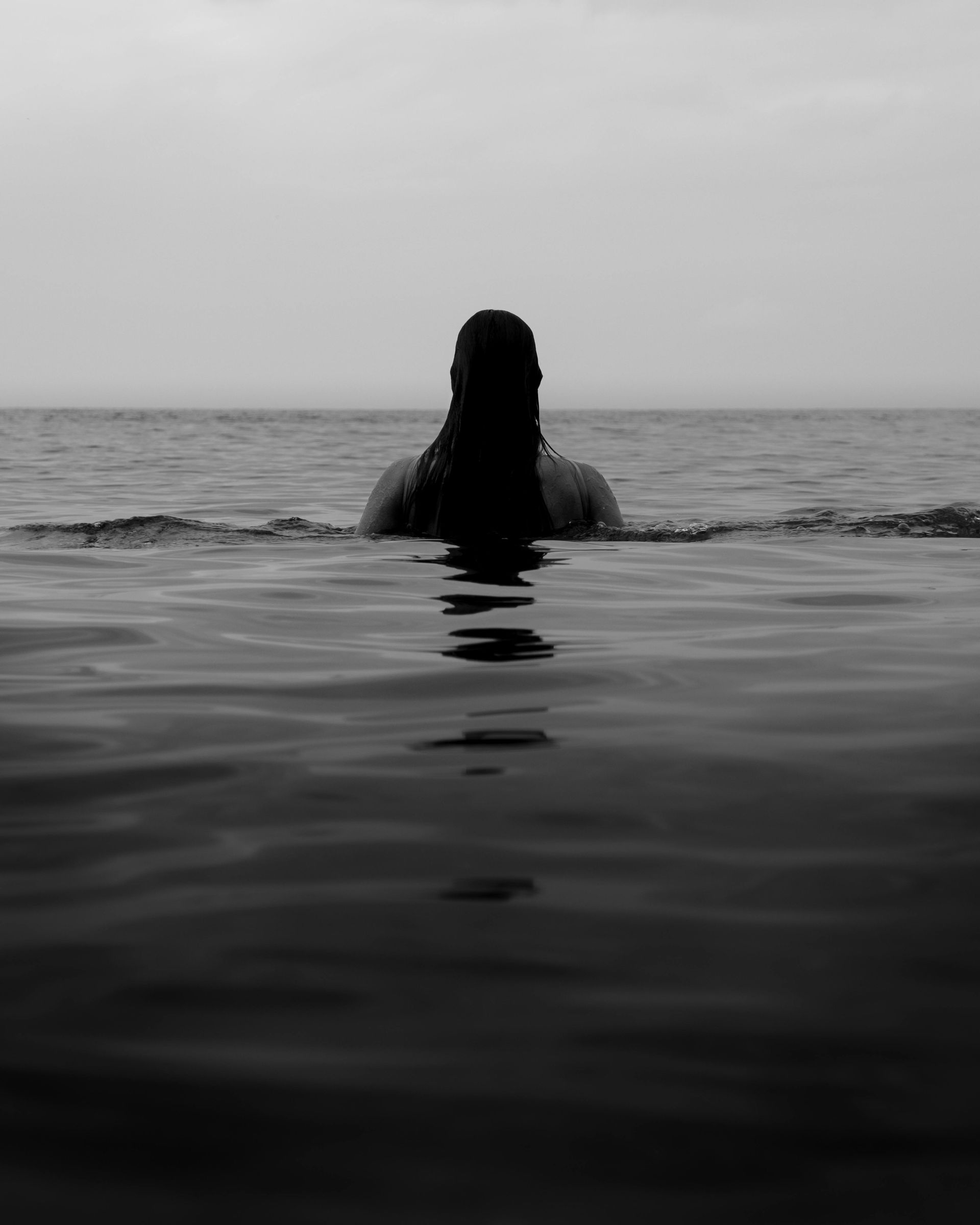 Ein schwarz weiß bild, auf dem eine Frau im Meer ist.