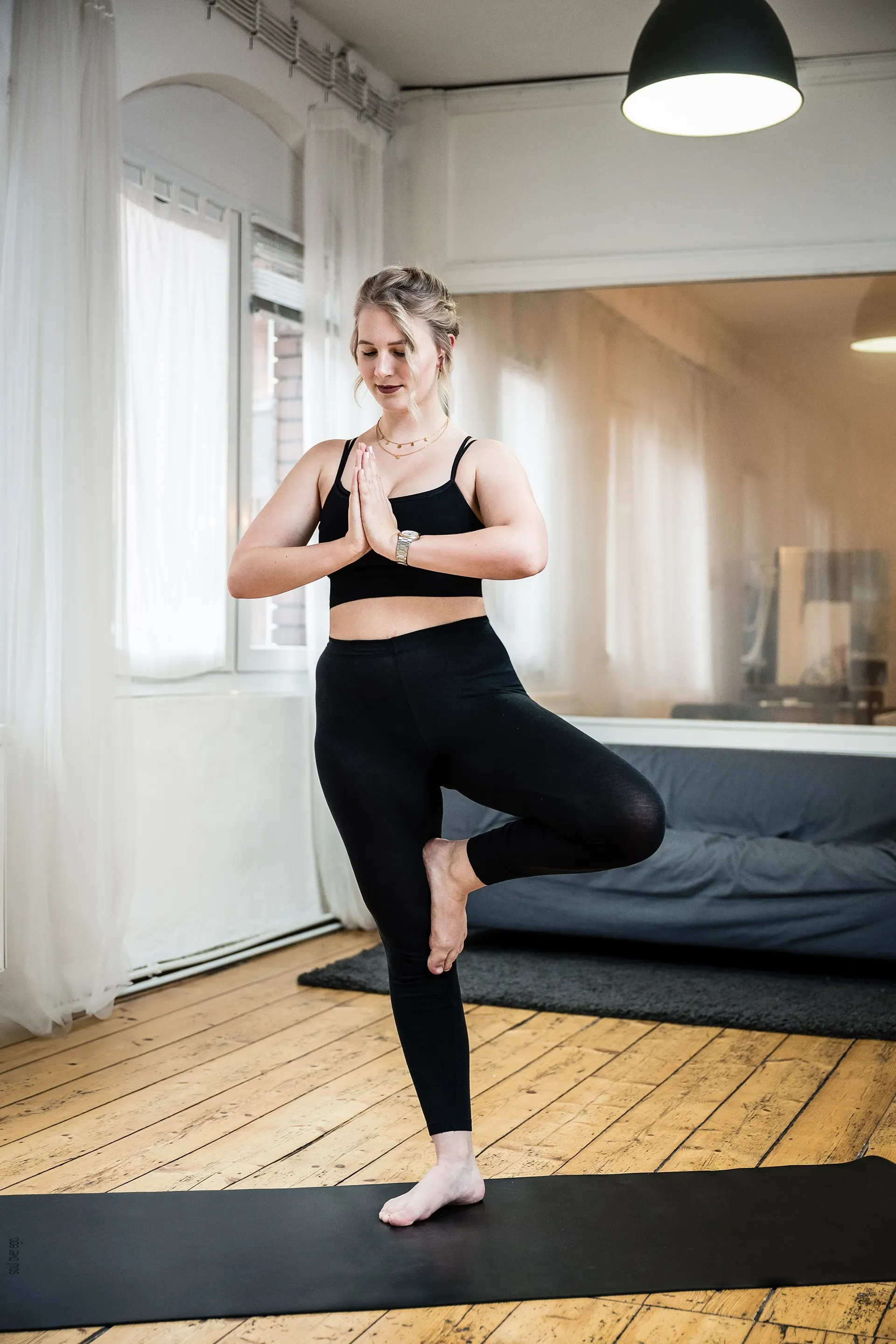 Eine Frau sitzt mit den Händen am Kopf auf einer Yogamatte und verneigt sich