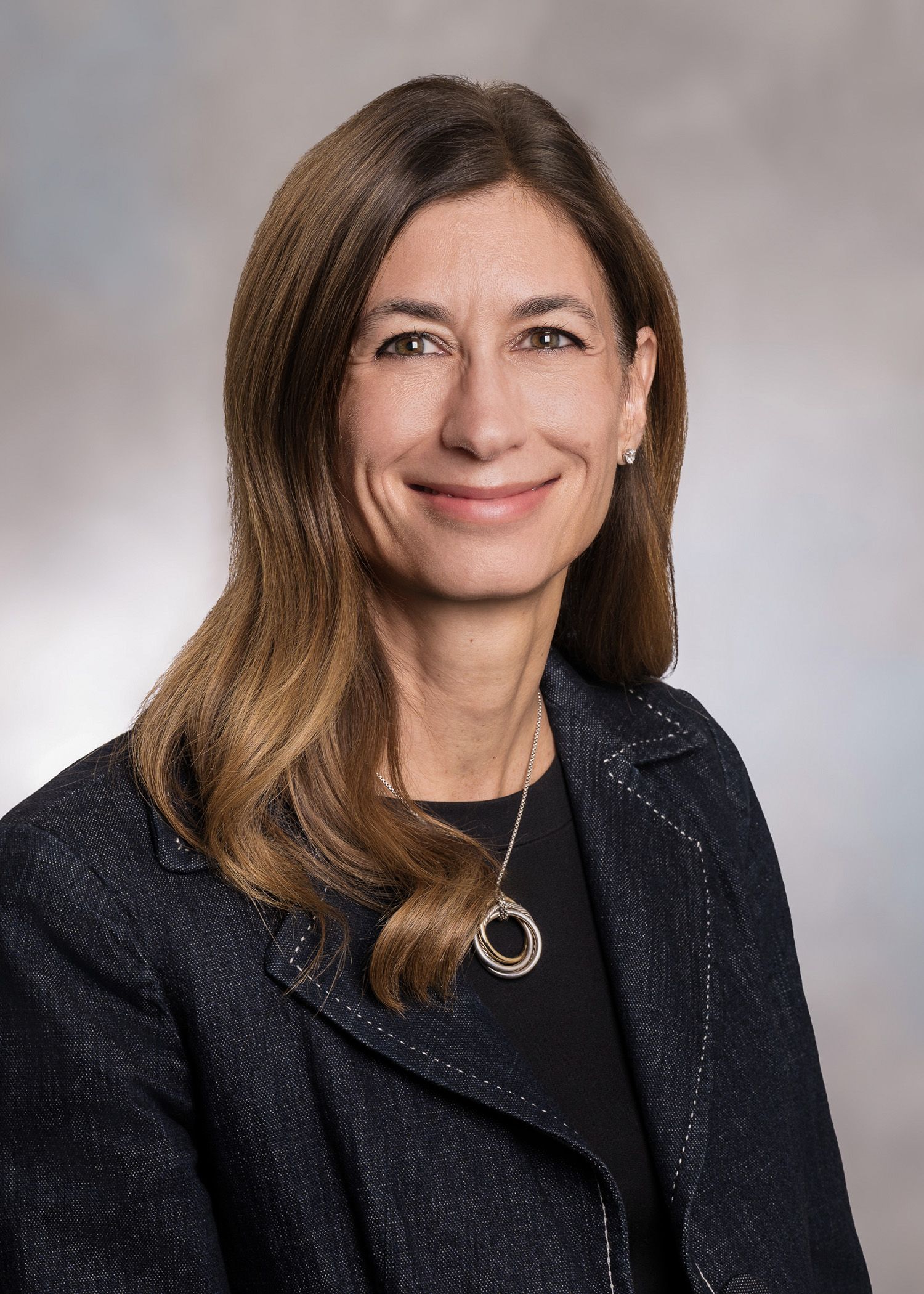 A woman wearing glasses and a white lab coat is smiling.