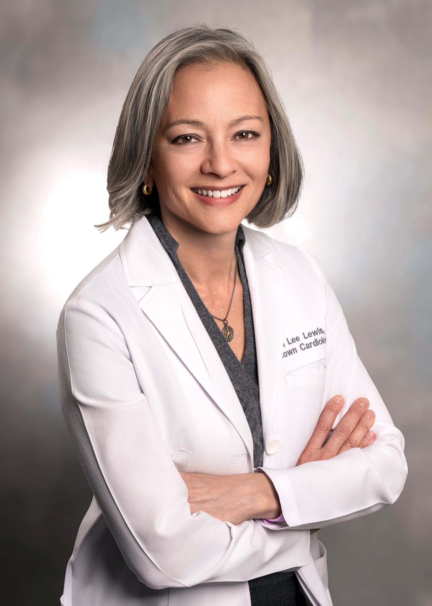 A woman in a white lab coat is smiling with her arms crossed.
