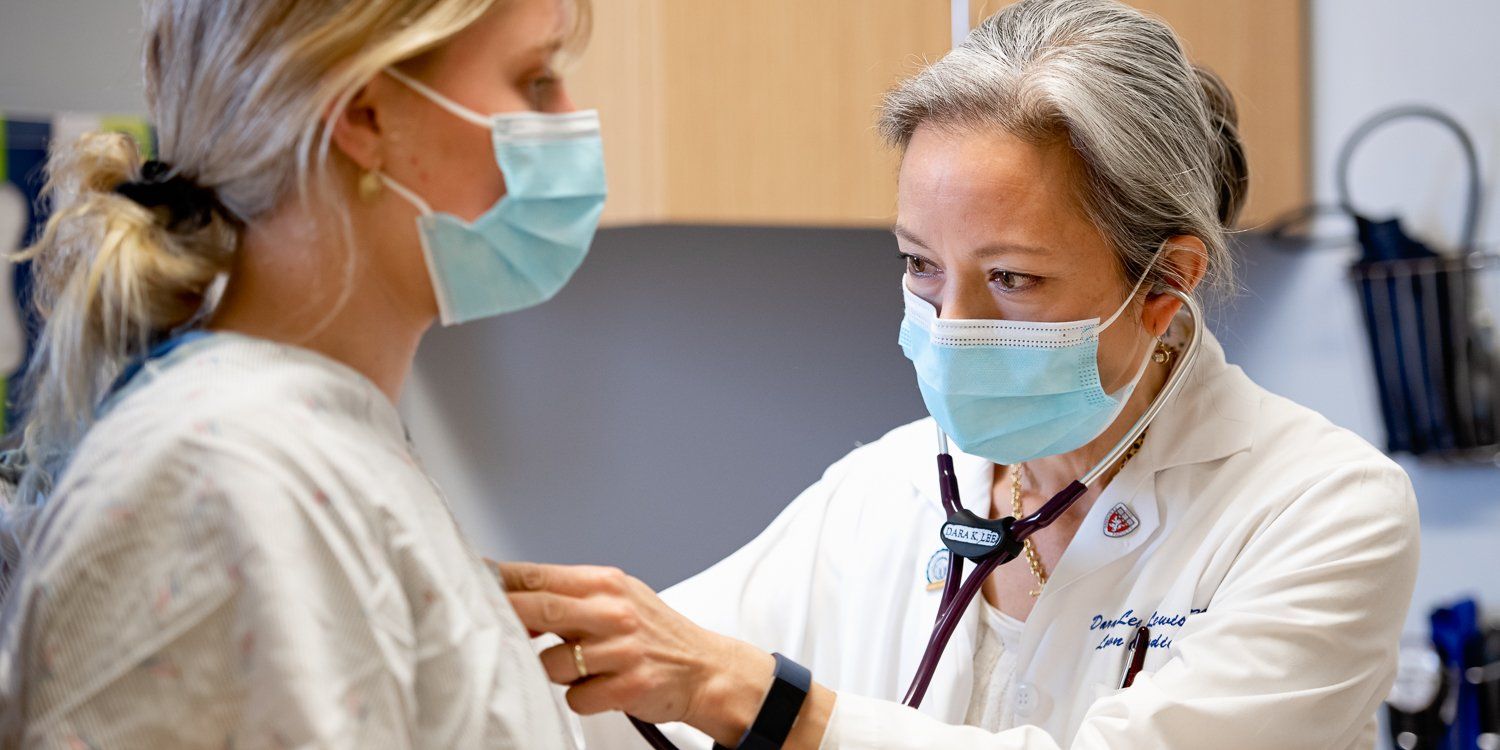 A doctor wearing a mask is listening to a patient 's heart with a stethoscope.
