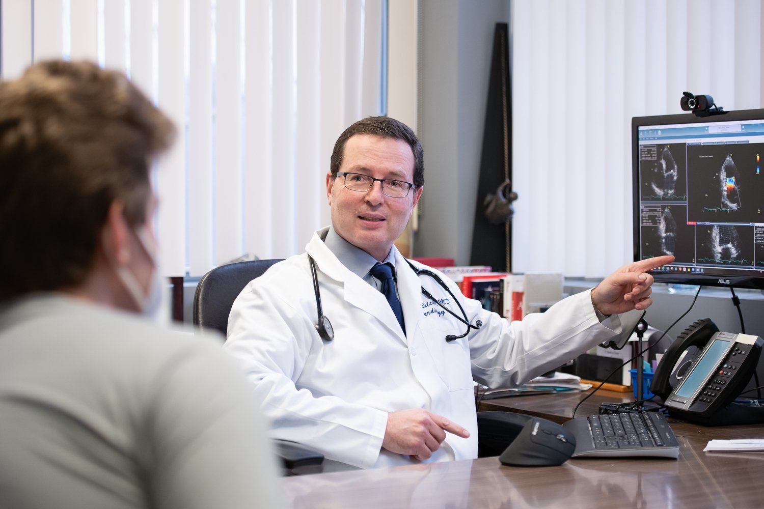 A doctor is sitting at a desk talking to a patient.