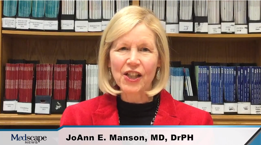A woman in a red jacket is standing in front of a bookshelf.