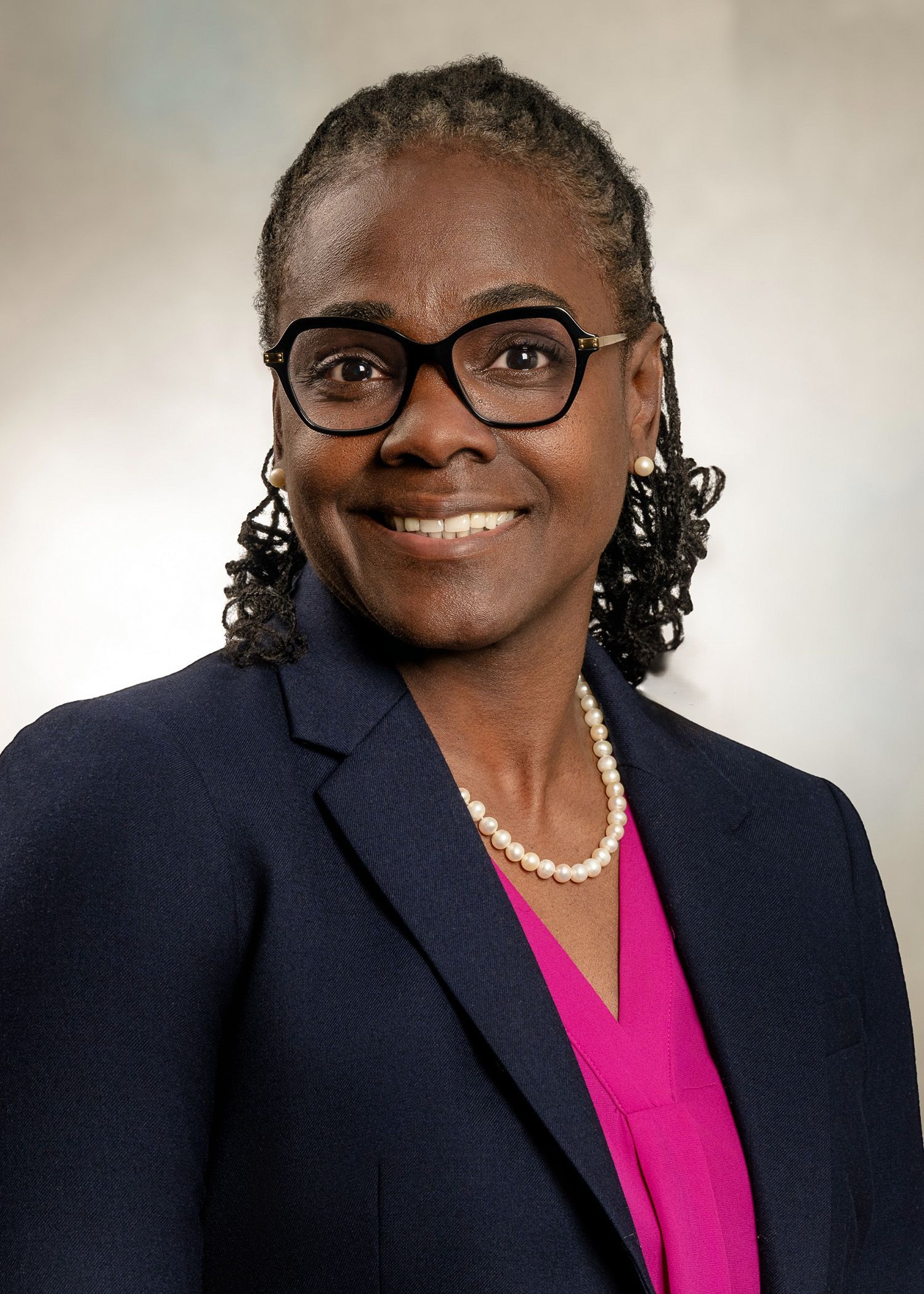 A woman wearing glasses and a pearl necklace is smiling for the camera.
