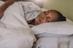 A woman is sleeping in a bed with white sheets and pillows.