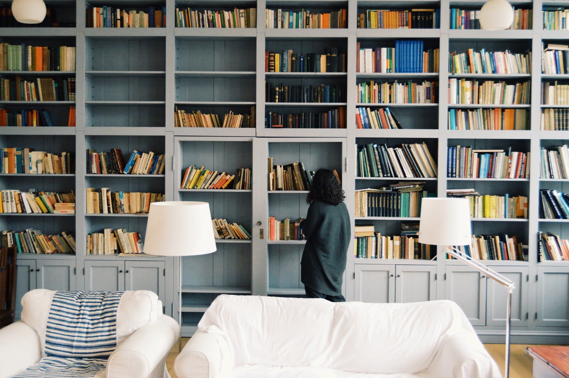 A woman is standing in front of a wall of bookshelves in a living room.