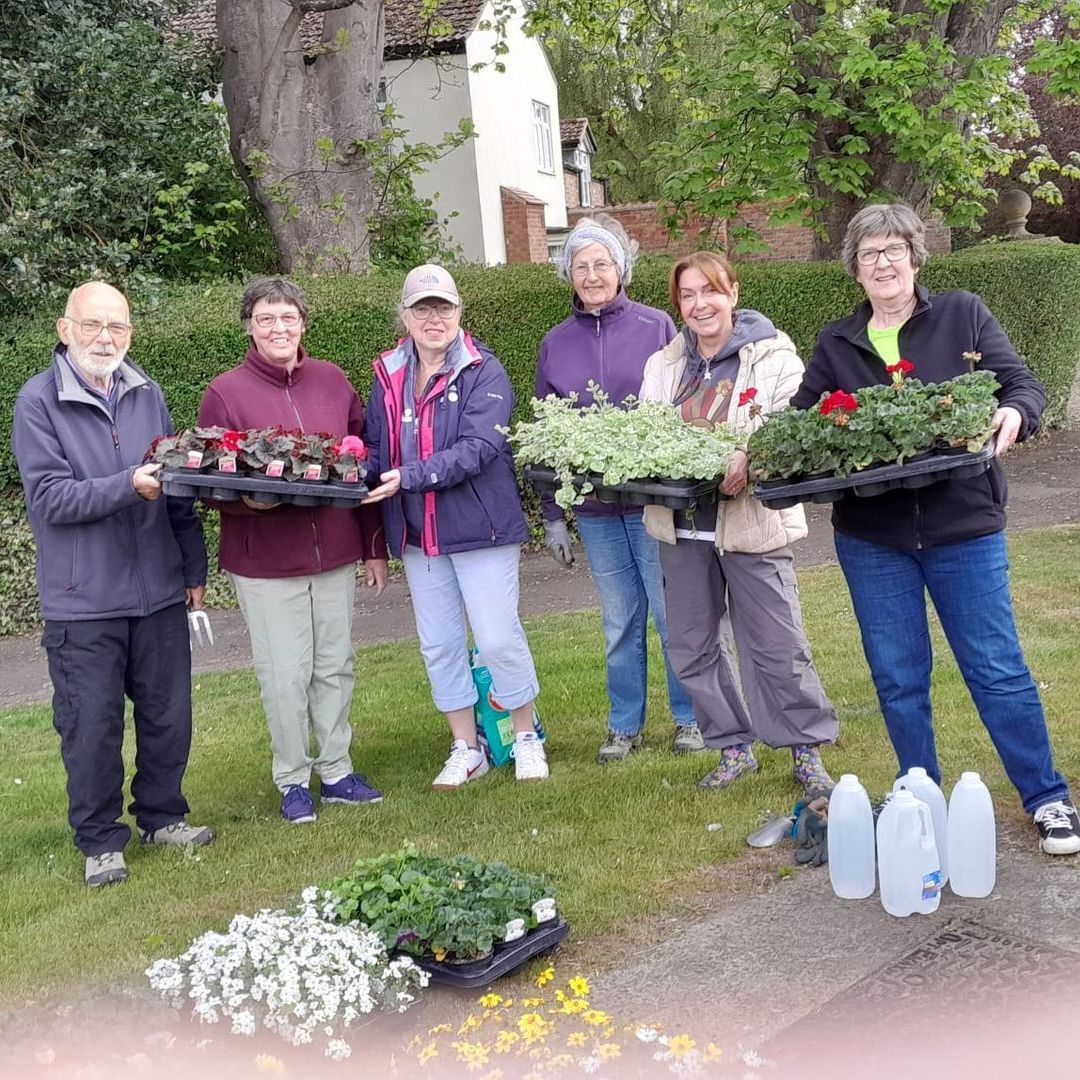 A group of people are standing in a park holding potted plants.