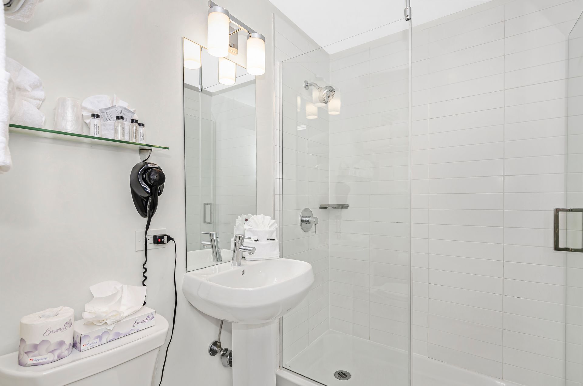 A modern, bright bathroom with a white pedestal sink, a glass-enclosed shower, and a mirror above the sink.