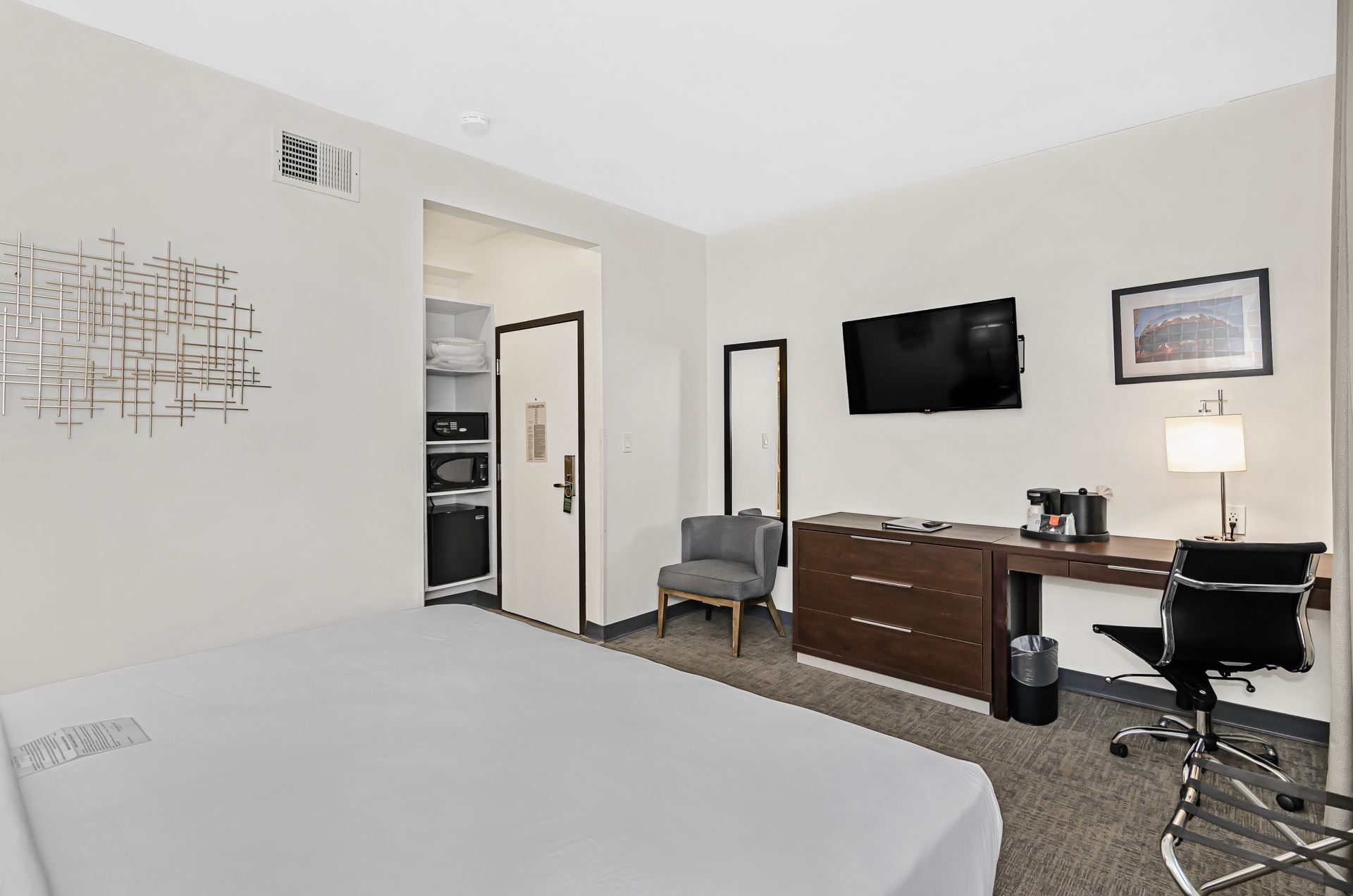 A hotel room with a bed, a desk, a television mounted on the wall, a chair, and a door leading to a closet area.