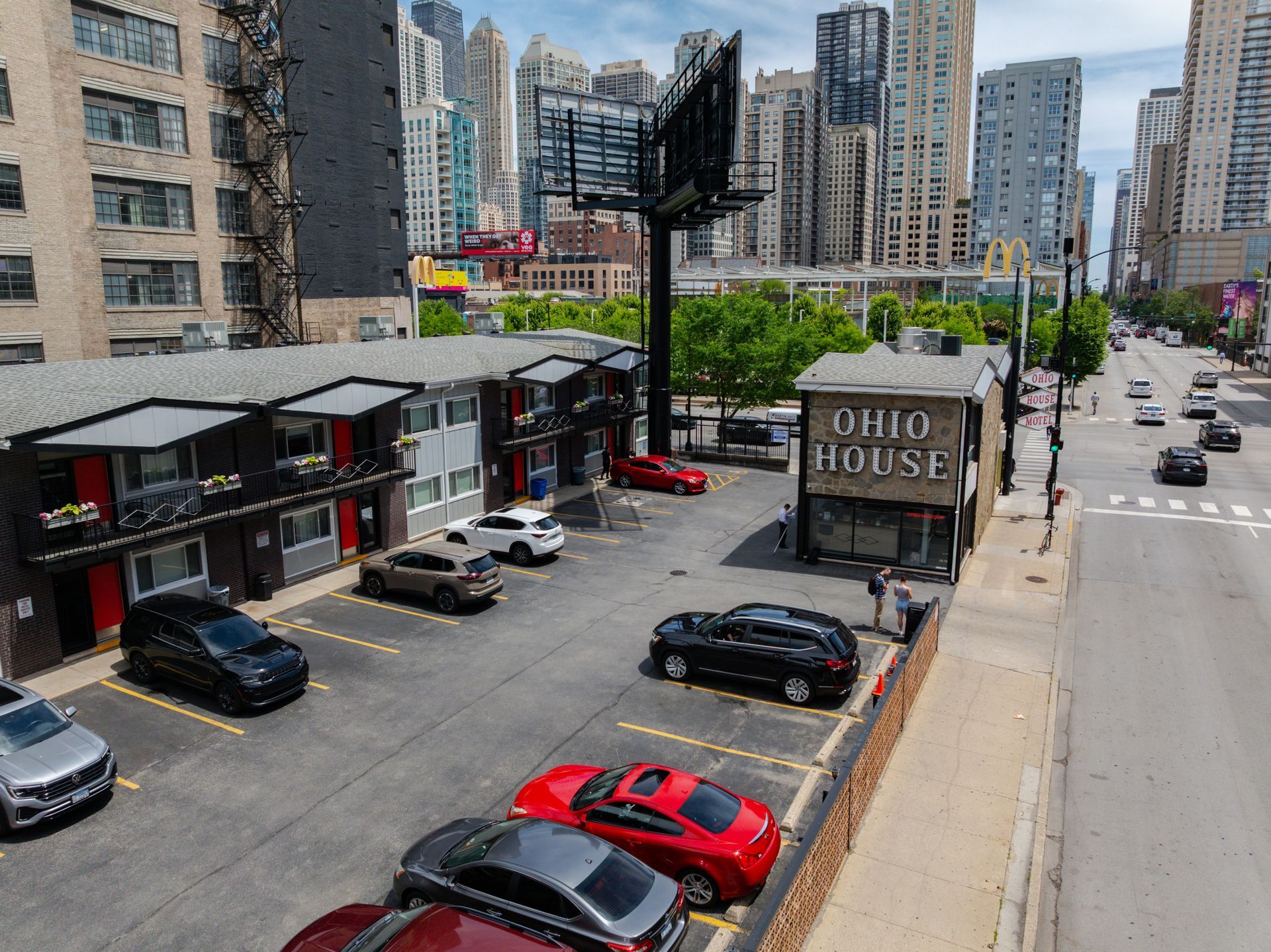 Urban parking lot beside tall apartment buildings, with several parked cars under a clear sky.
