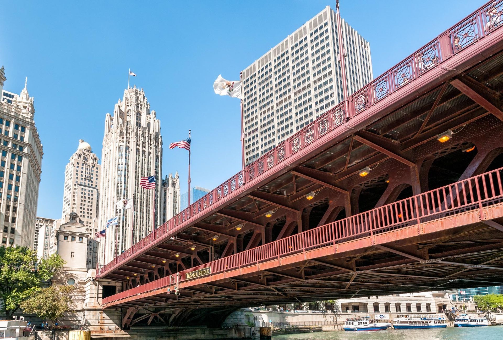Red bridge over Chicago River with city buildings and blue sky.