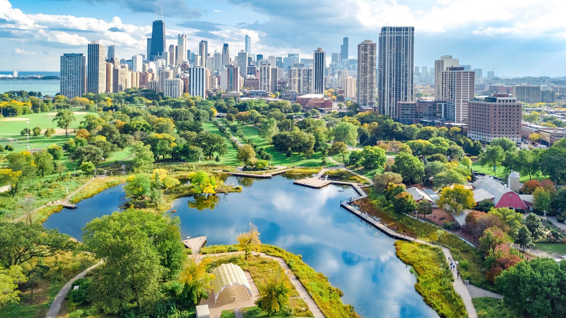 Chicago skyline view over a green park and blue lake. Sunny day, skyscrapers, trees, and walking paths.