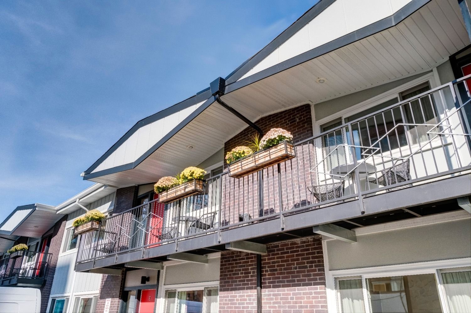 Balconies with brick and grey siding, yellow flowers in planters, blue sky.
