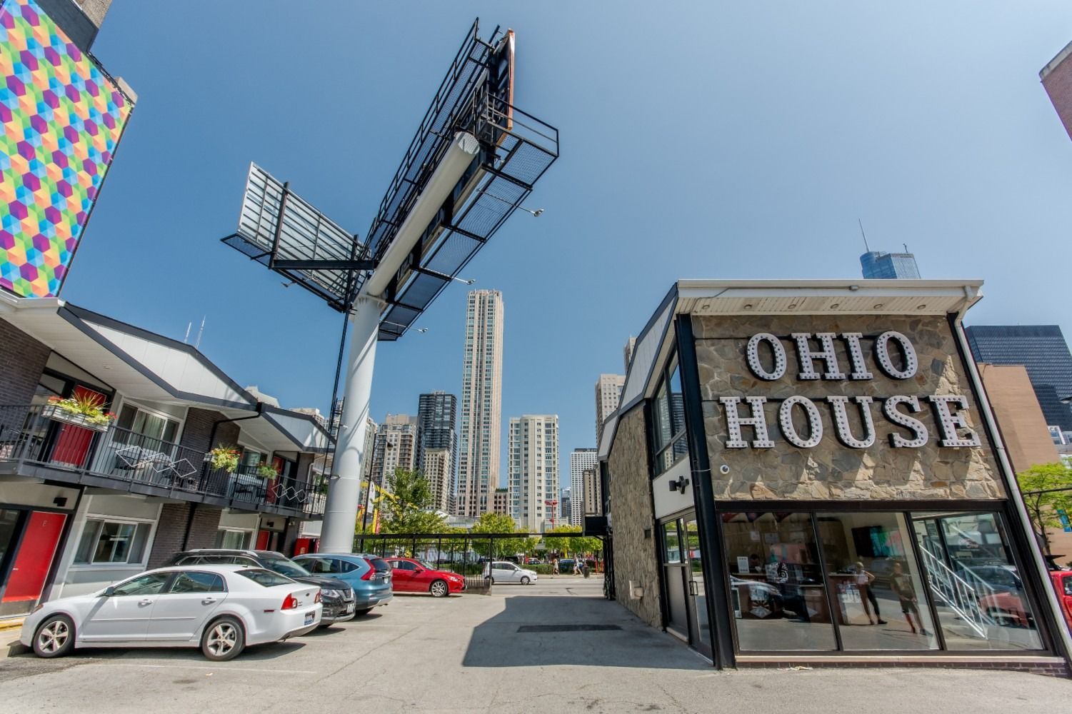 Ohio House sign on building with cars parked in front, with large billboard and city skyline in the background.