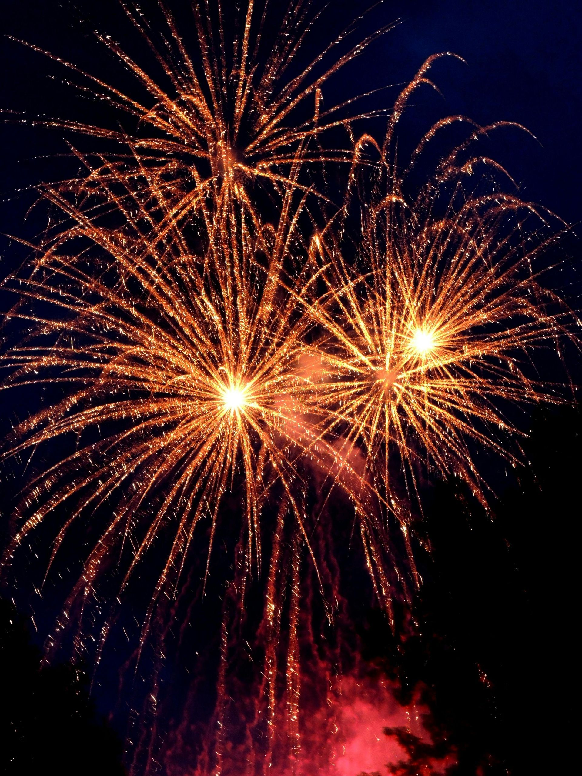 Bright gold fireworks burst in a dark night sky, with a faint red glow visible at the bottom.
