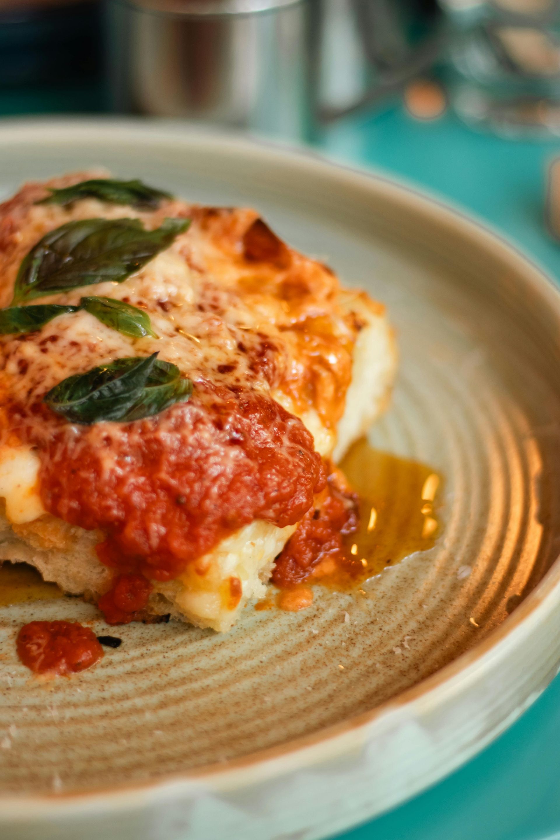 A piece of golden-brown chicken parmigiana topped with melted cheese, tomato sauce, and fresh basil on a ceramic plate.