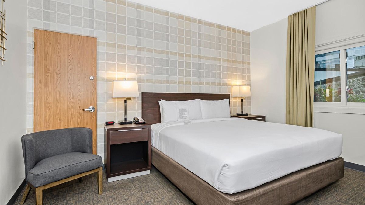 Hotel room with a double bed, bedside tables, lamps, a chair, and a window.