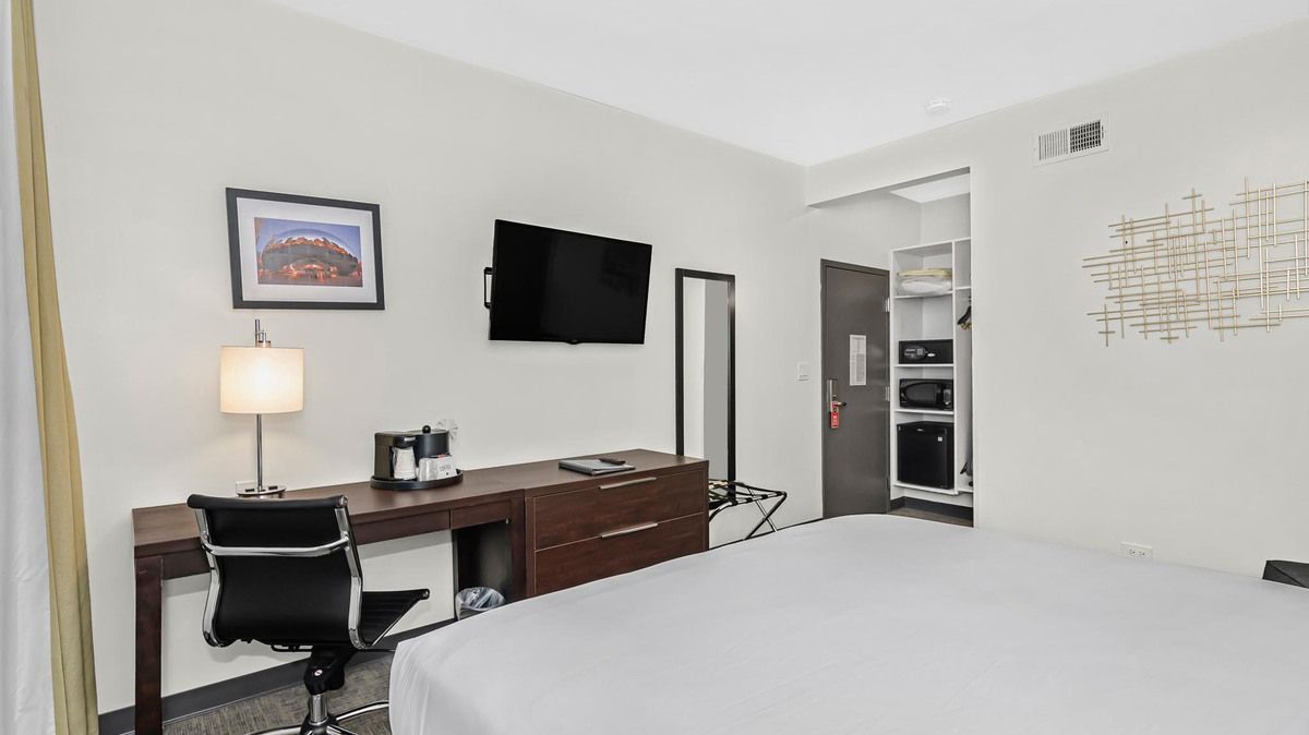 Hotel room with bed, desk, TV, artwork, and closet.