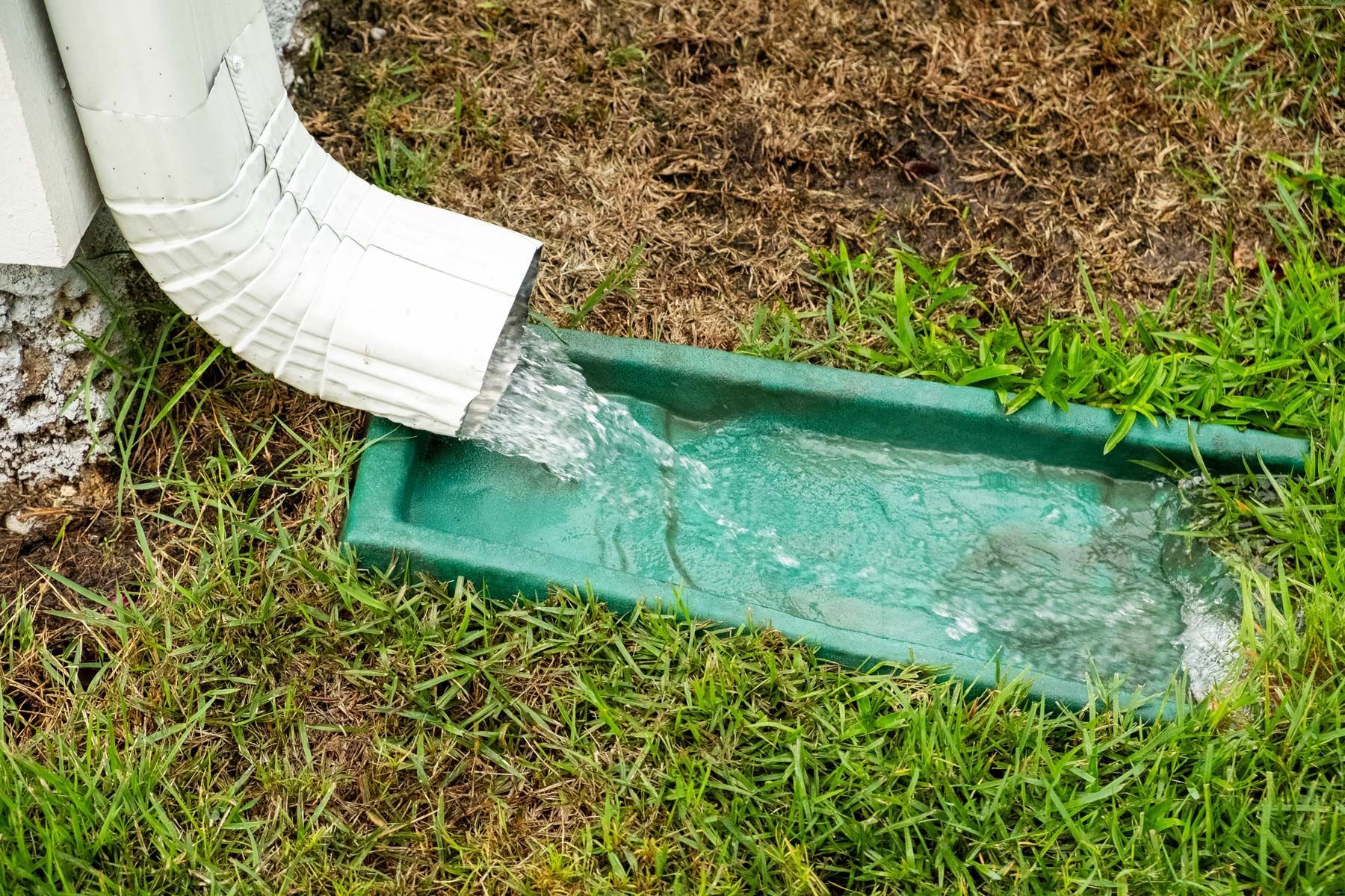 White gutter pouring water into a green channel on grass.