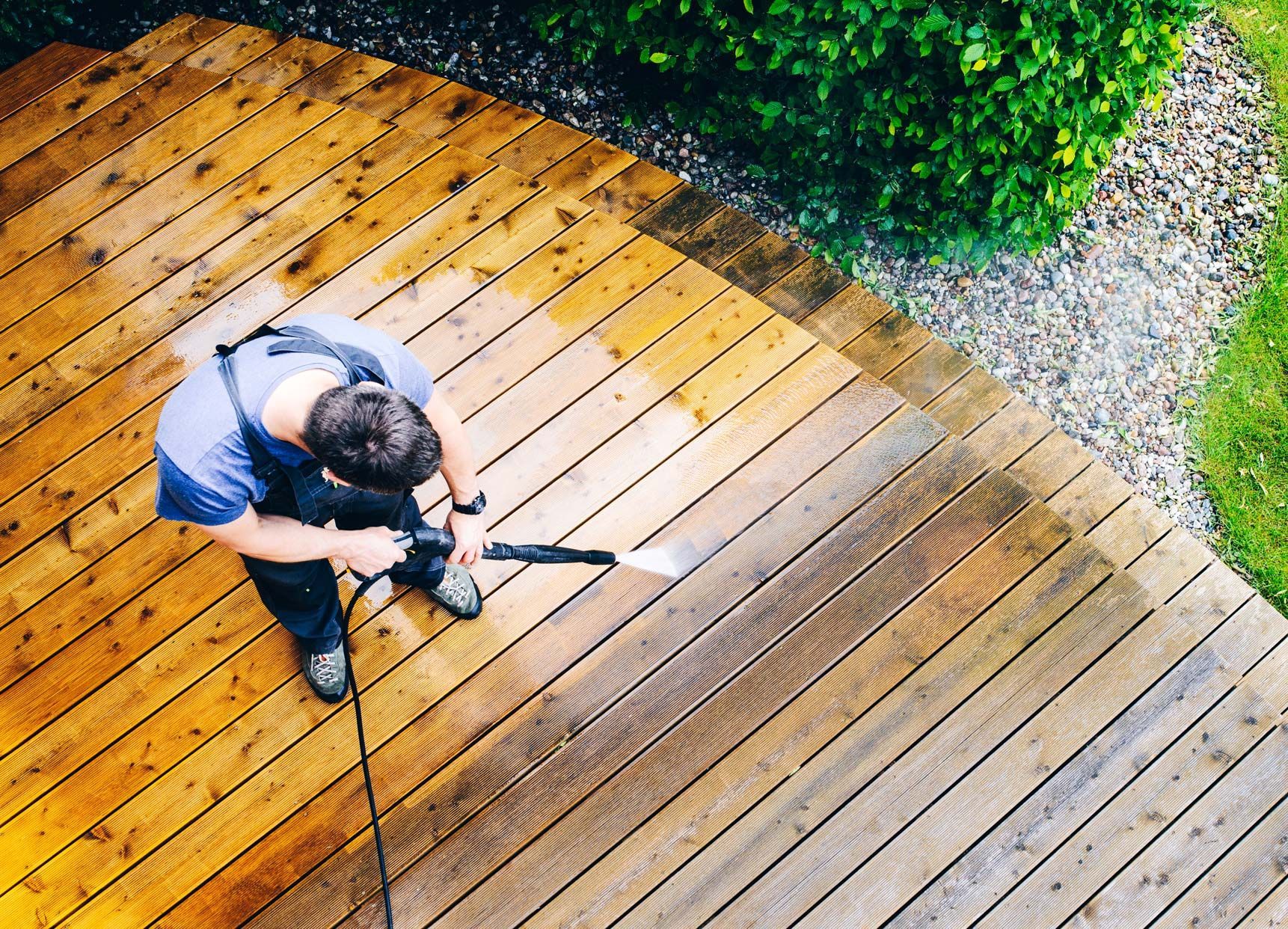 Person power washing a wooden deck, cleaning the surface with a high-pressure spray.