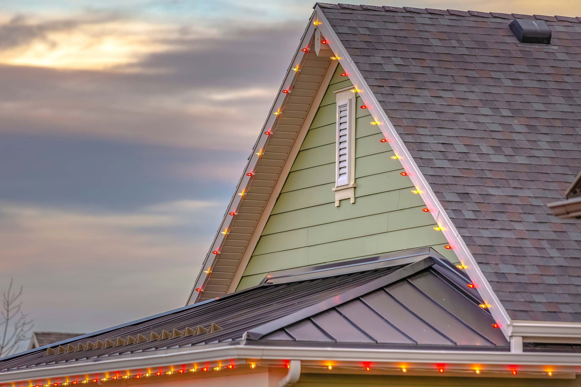 House with colorful Christmas lights along roof edges against a cloudy sky.