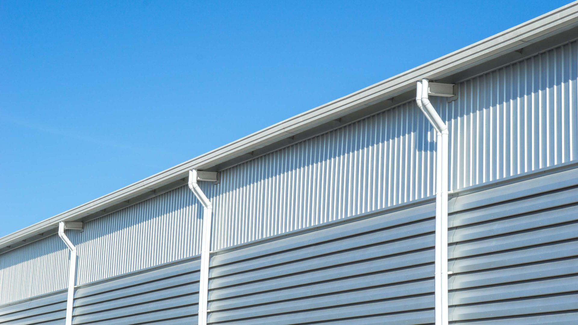 Corrugated metal building exterior with white gutters against a clear blue sky.