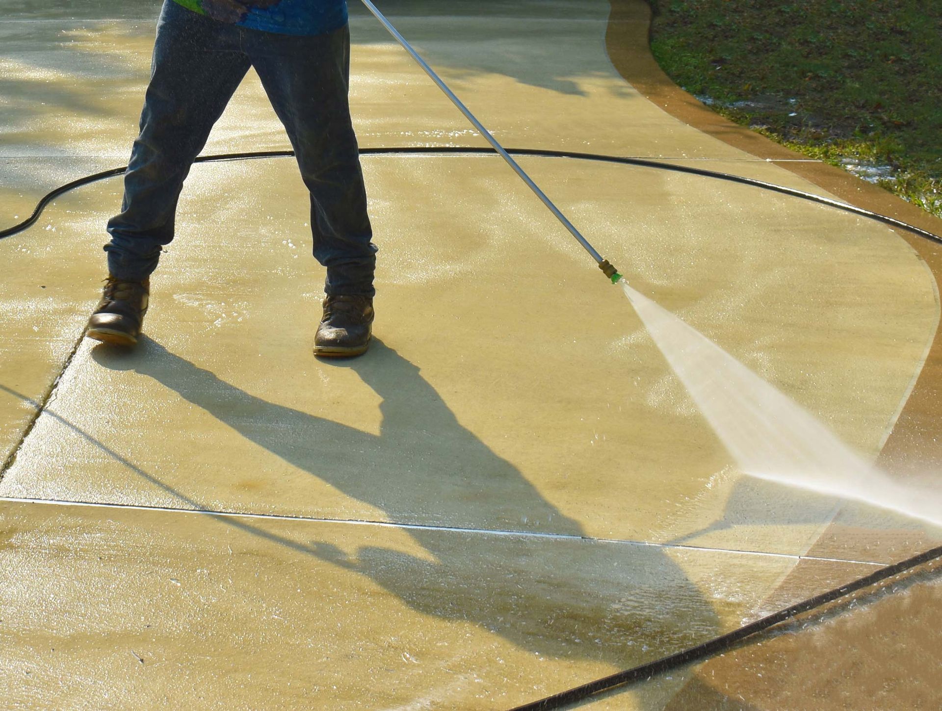 Person power washing a concrete driveway. Spraying water and creating a clean path. Sunny day.