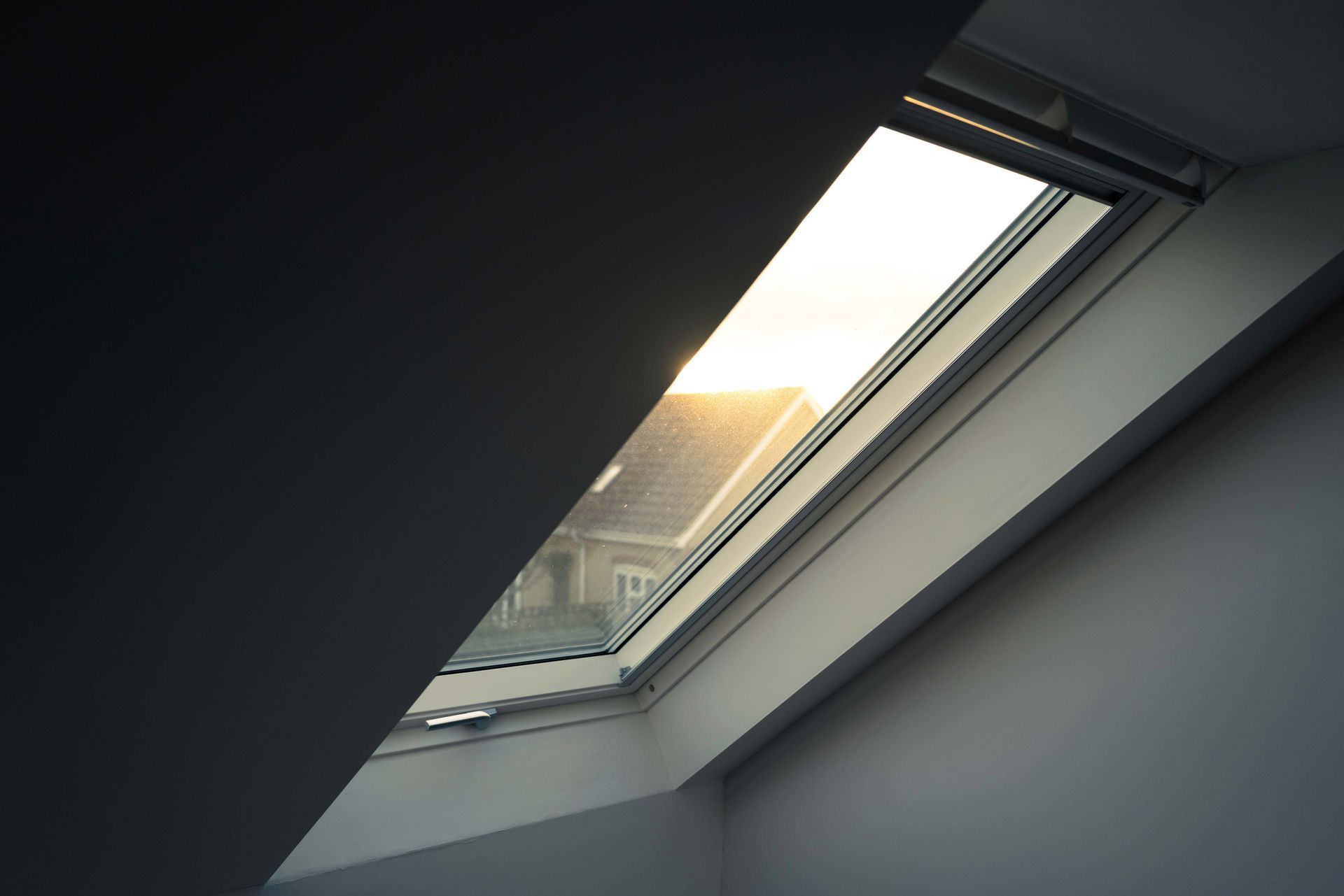 Skylight window in angled ceiling, with sunlight shining through to an exterior roof.