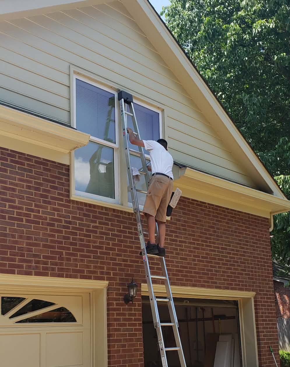 Person on a ladder cleaning a window on a brick house. Sunny day.