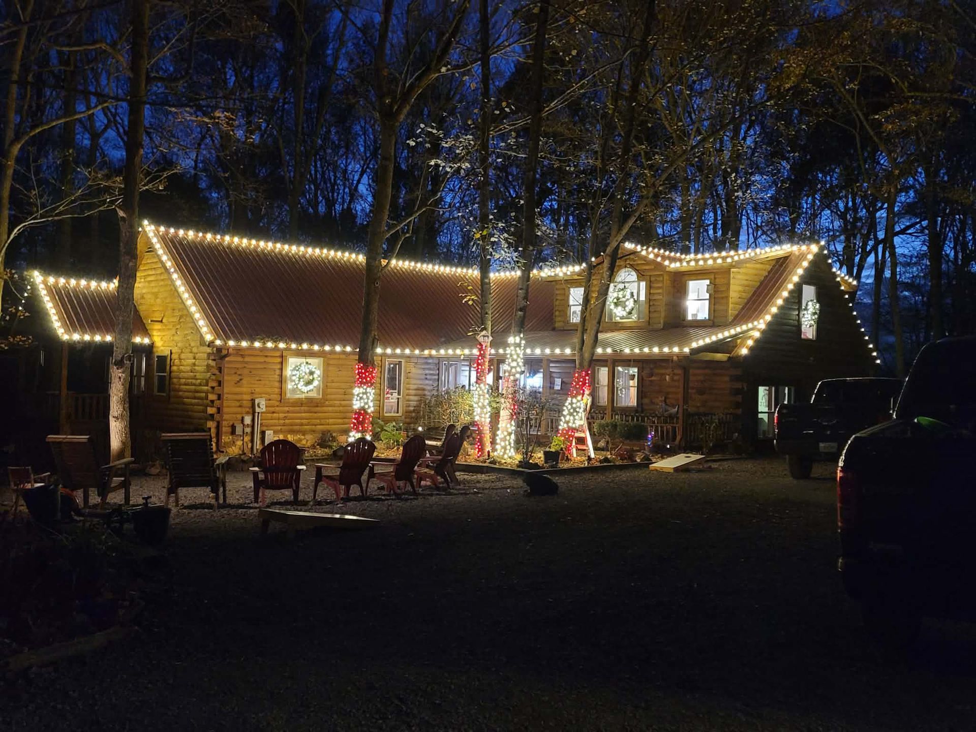 Log cabin with bright white Christmas lights, outdoor chairs. Dark setting.