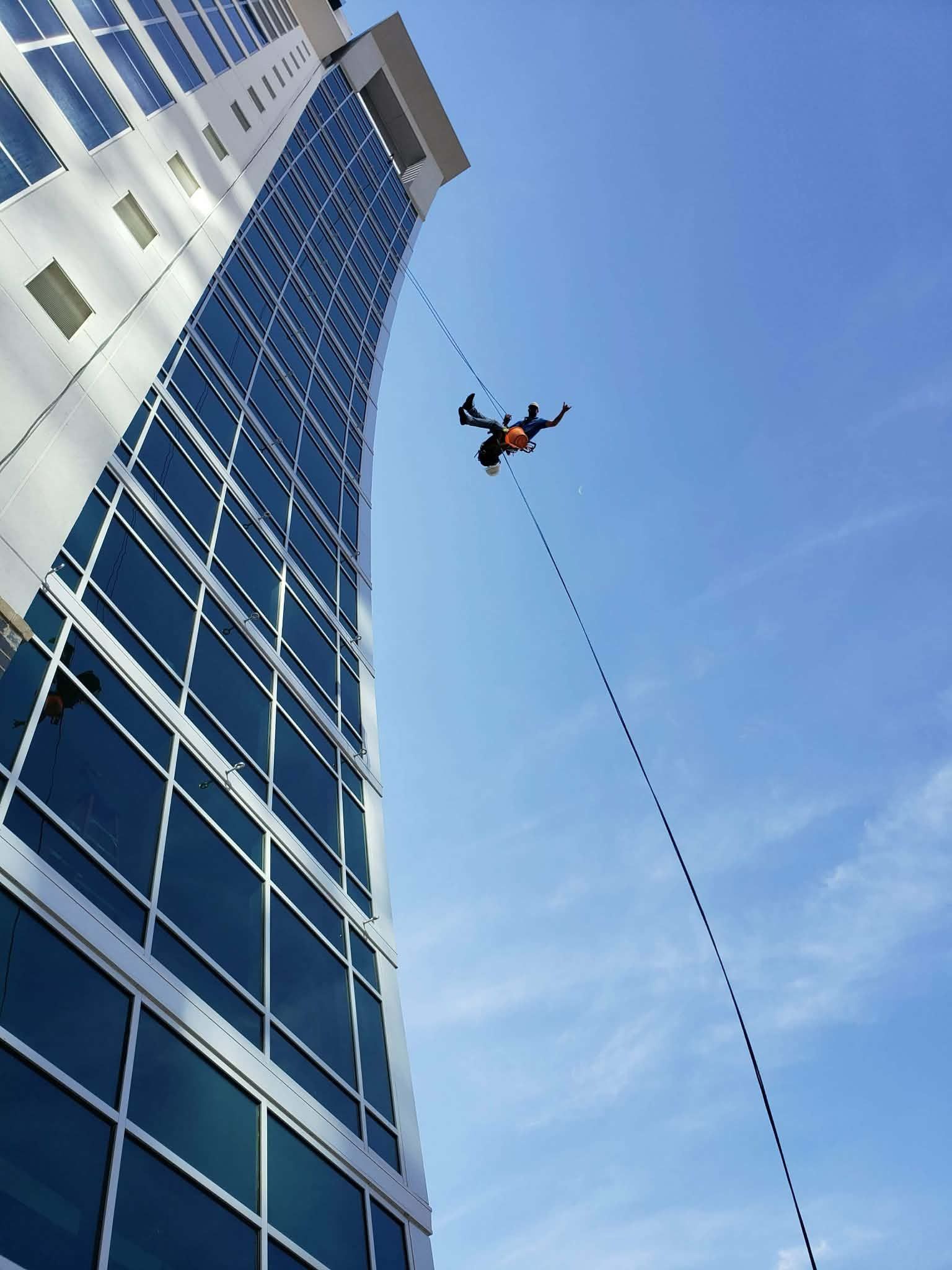 A person BASE jumping from a tall, glass skyscraper against a blue sky.