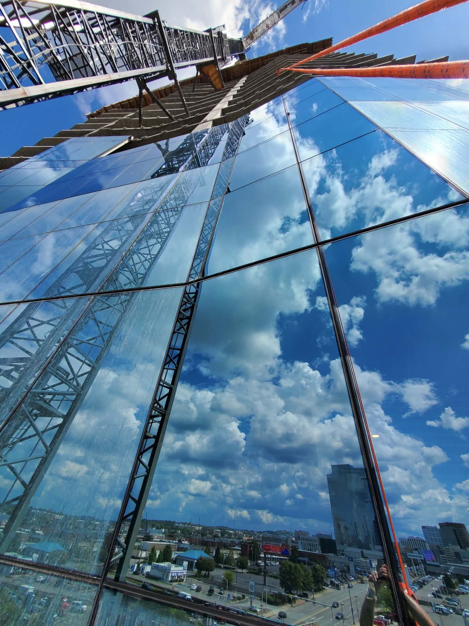 View up a mirrored skyscraper reflecting the sky, clouds, and cityscape below.