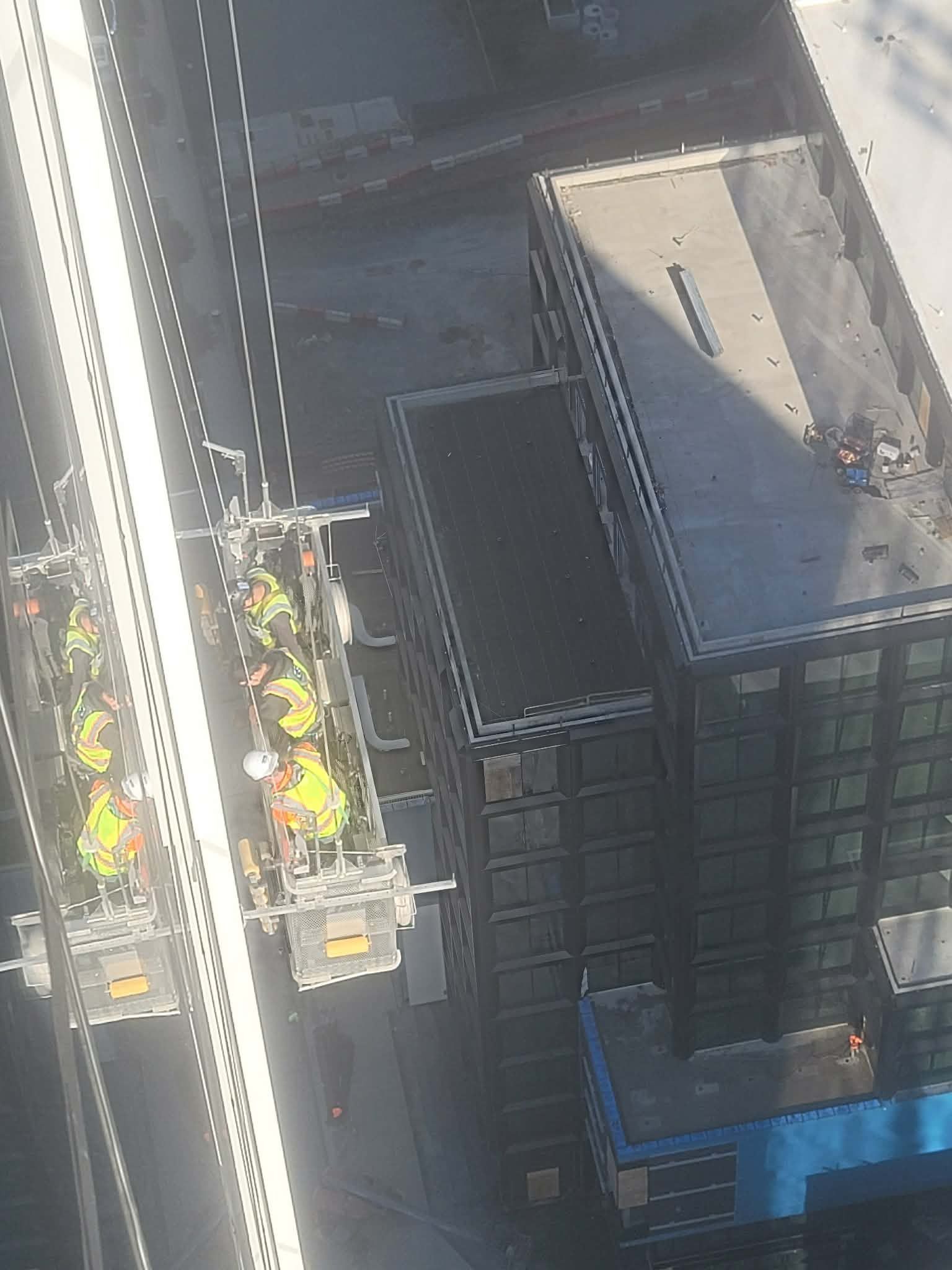 Overhead view of two work platforms on a road with a building. Platforms hold equipment and workers.