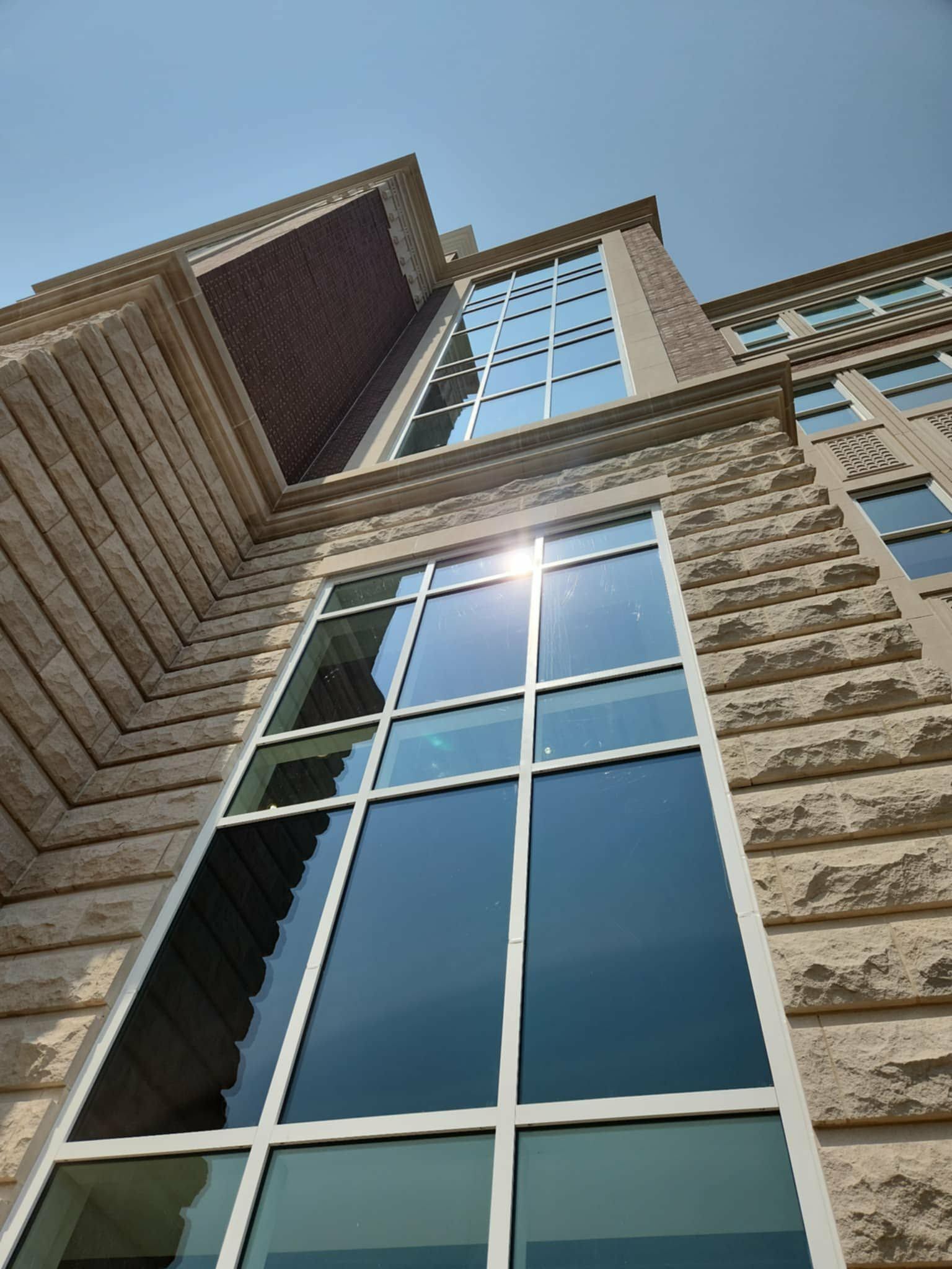 Low-angle view of a stone building with tall, reflective windows under a clear, sunny sky.