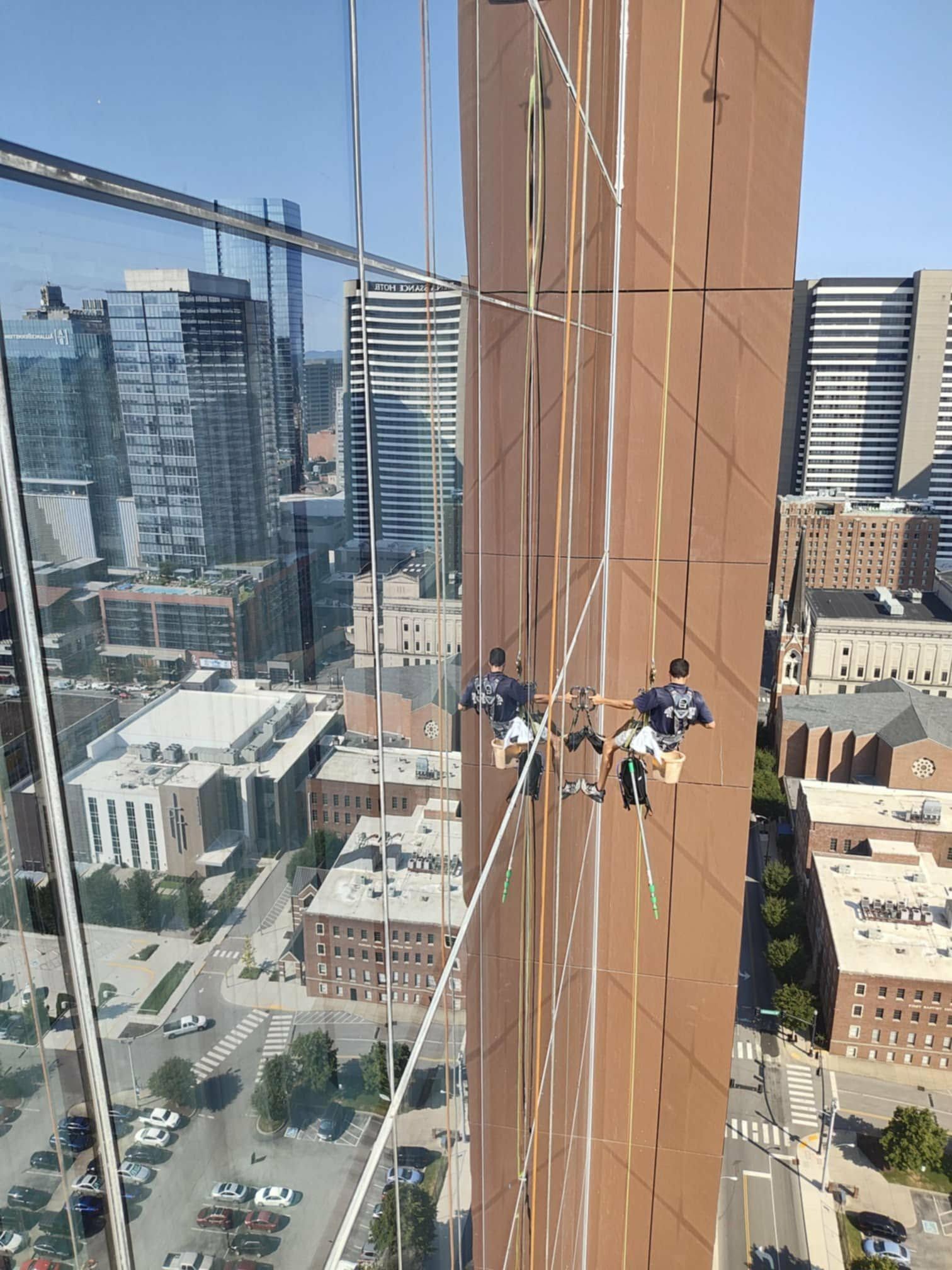 Two window washers suspended on ropes cleaning a tall skyscraper in a city.