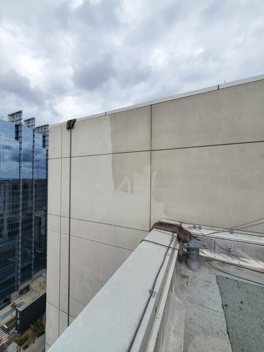 View from a high rooftop of a concrete building on an overcast day, with a glass building in the distance.