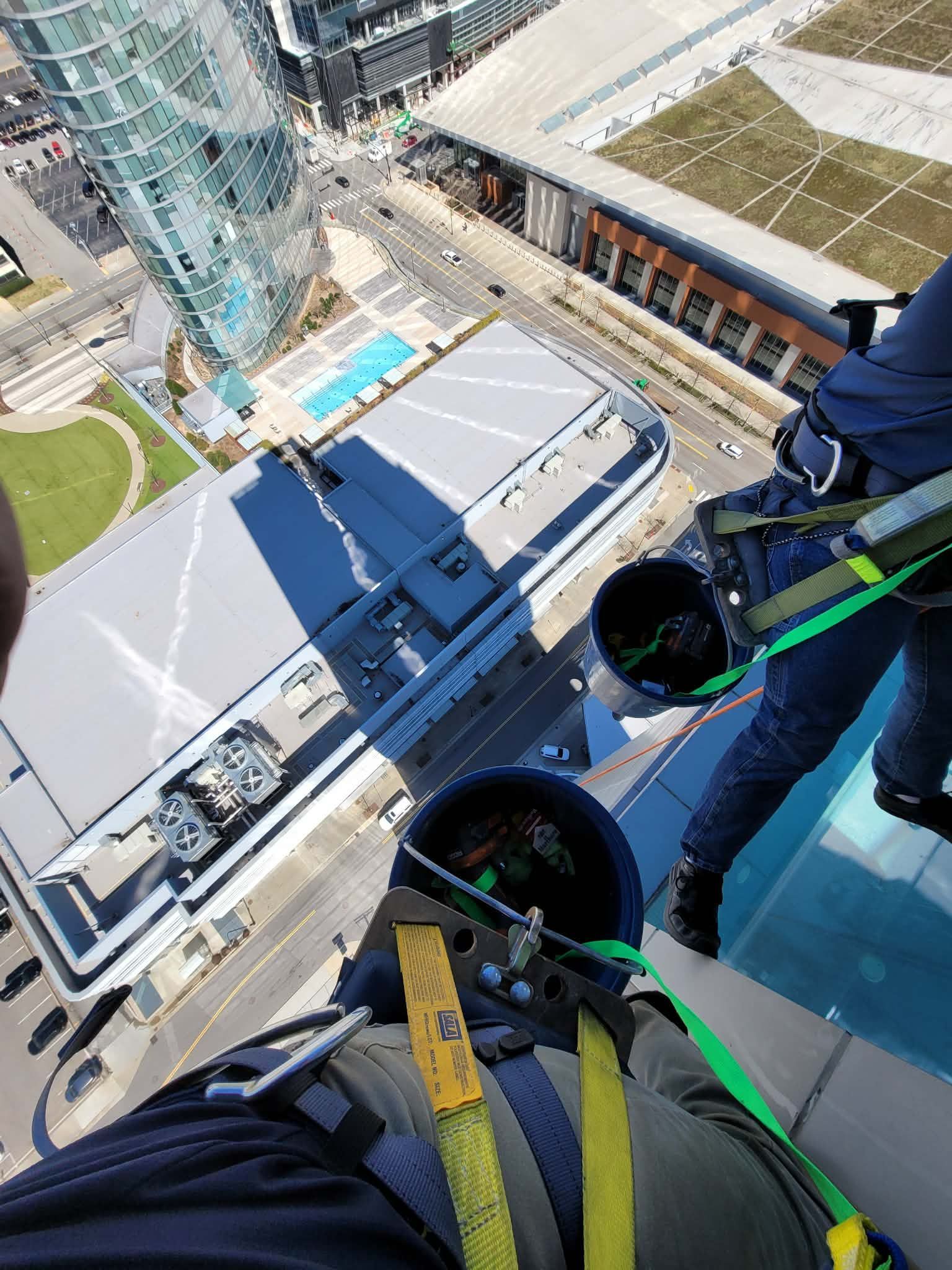 Person rappelling down a tall building, seen from a high angle. City buildings and street below.
