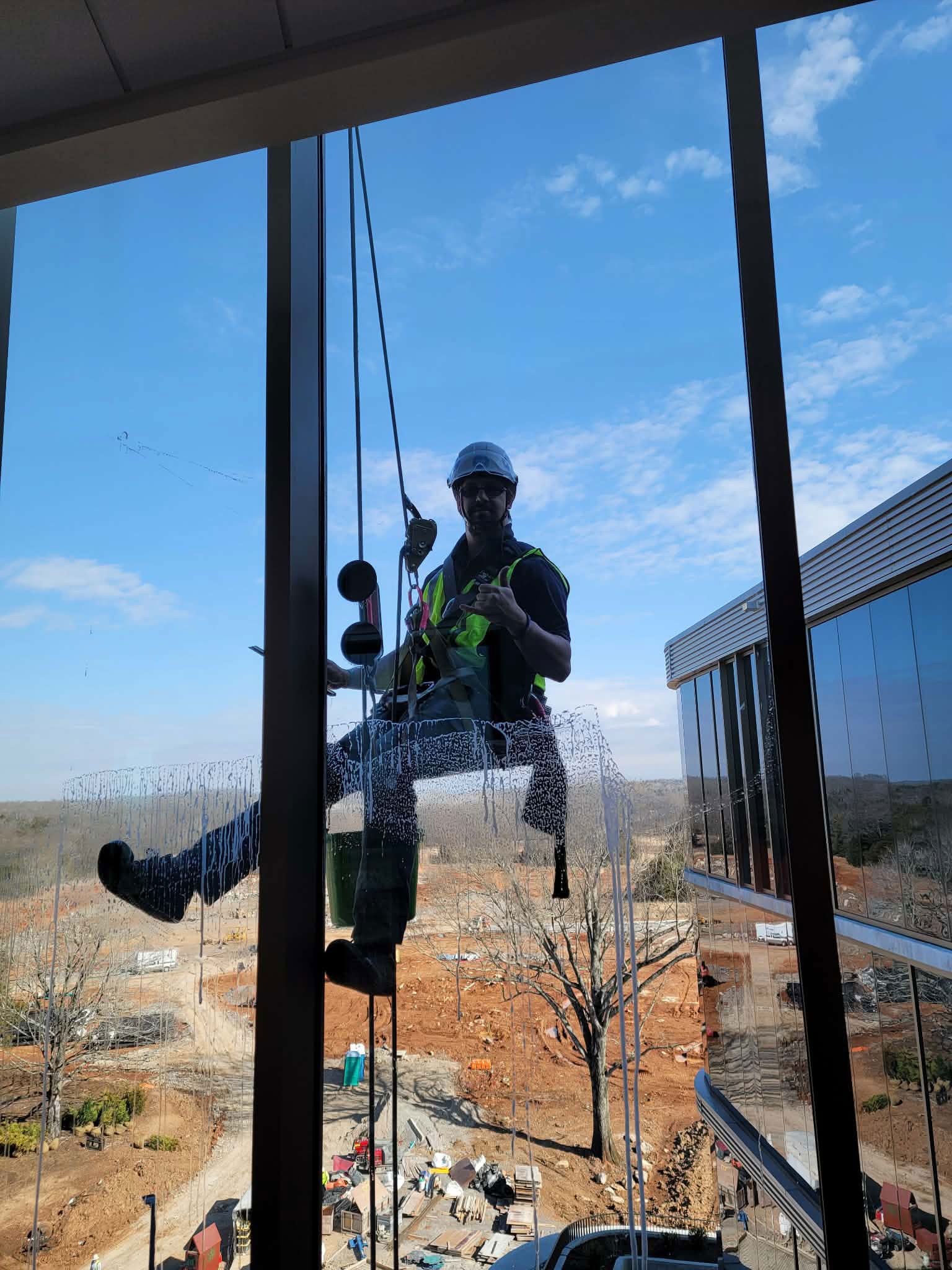 Window cleaner suspended on ropes, working on a glass building exterior. Sunny day, blue sky.