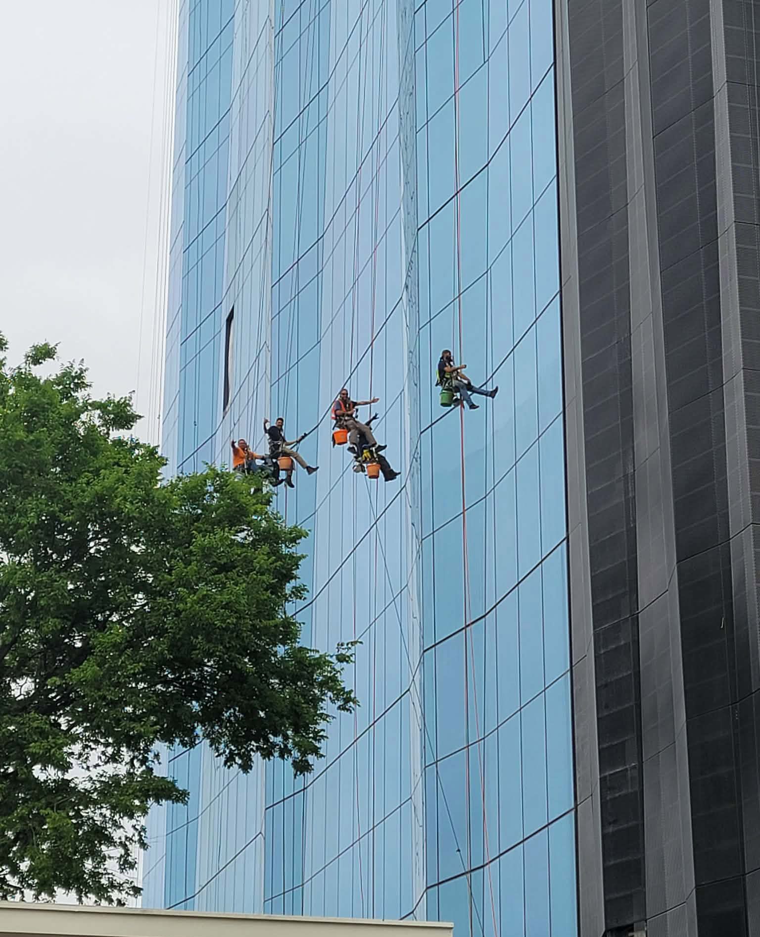 Workers on scaffolding washing windows of a tall, blue glass building.
