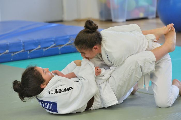 Due atleti di judo in kimono bianco si allenano su un tatami al chiuso.