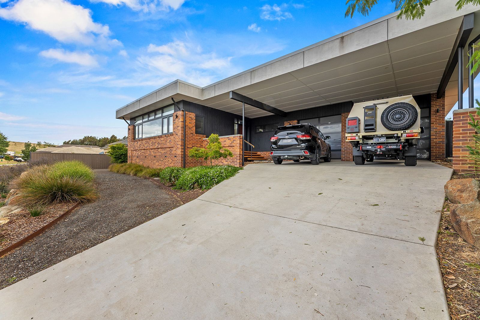 A single-story modern home with a covered car parking area. A car and motorcycle are parked.