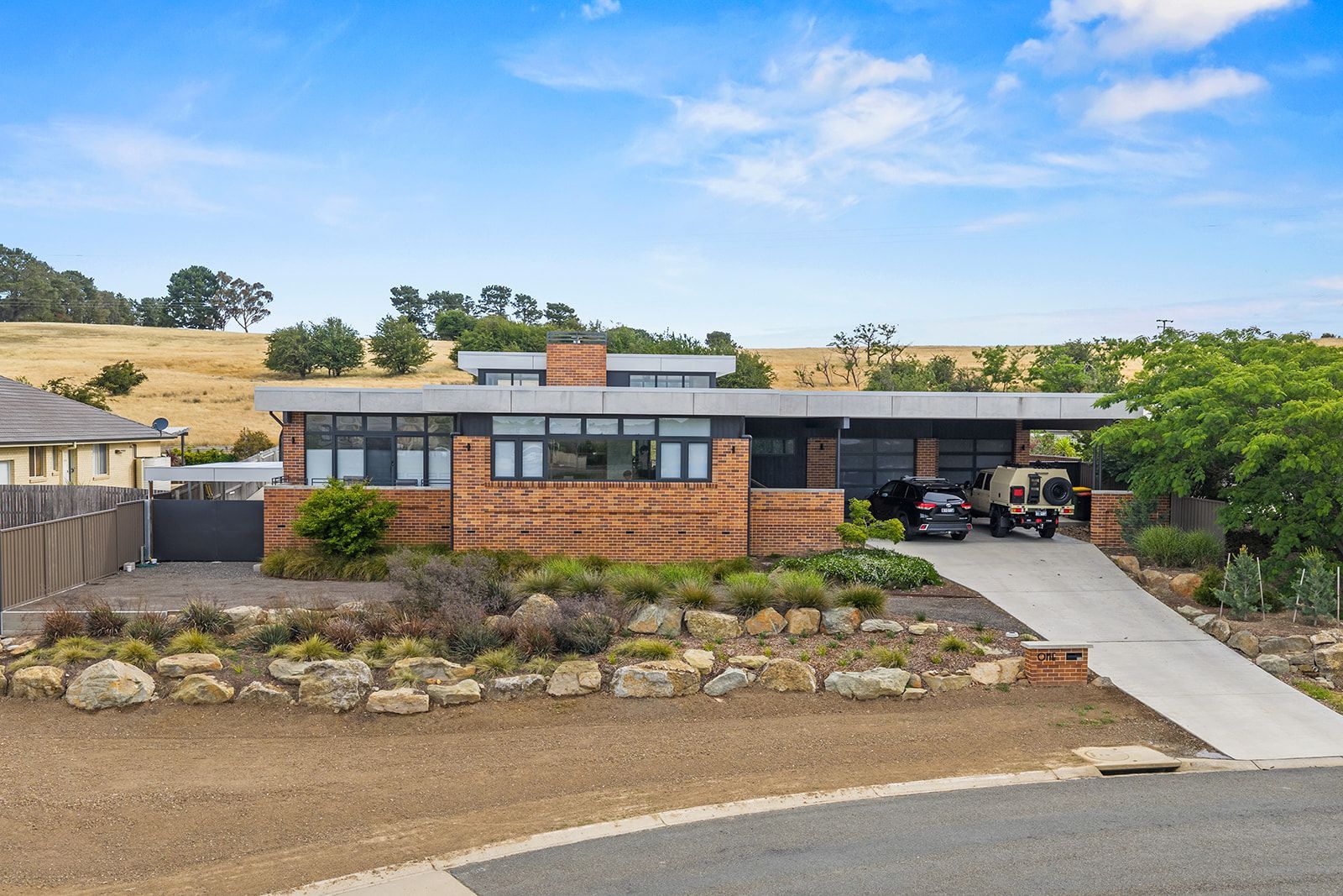 Modern brick house with flat roof and garage, driveway sloping up, and dry landscaping.
