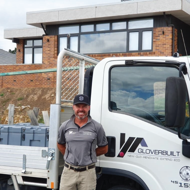 Anthony in front of a white truck with "Gloverbuilt" logo and a building in the background.