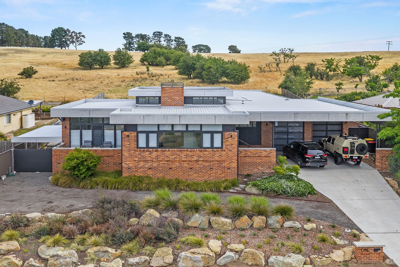Brick and flat-roofed house with a two-car garage, driveway, and arid hillside backdrop.