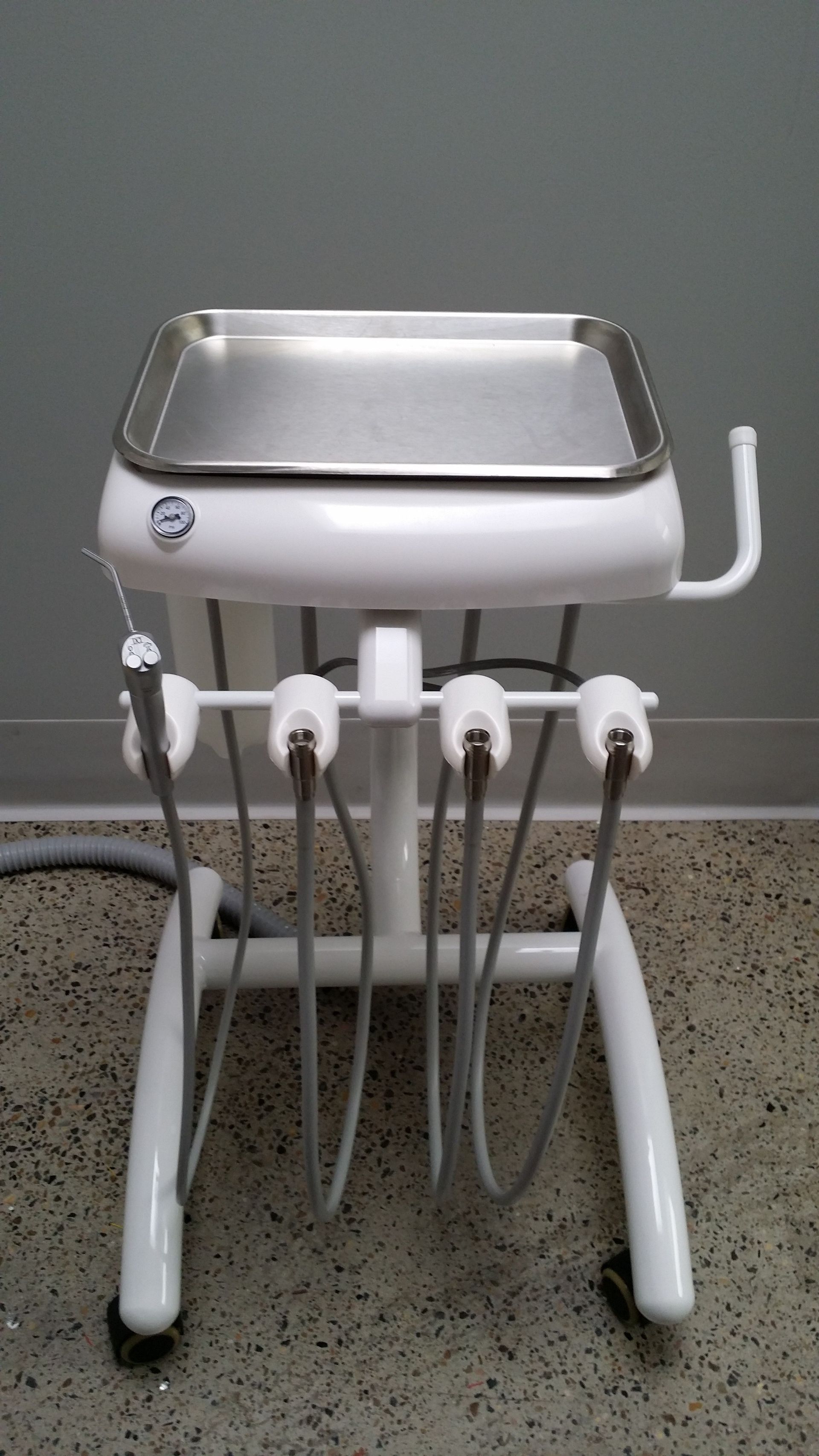 White dental assistant's cart with stainless steel tray, containing handpieces and other dental tools, in a medical office.