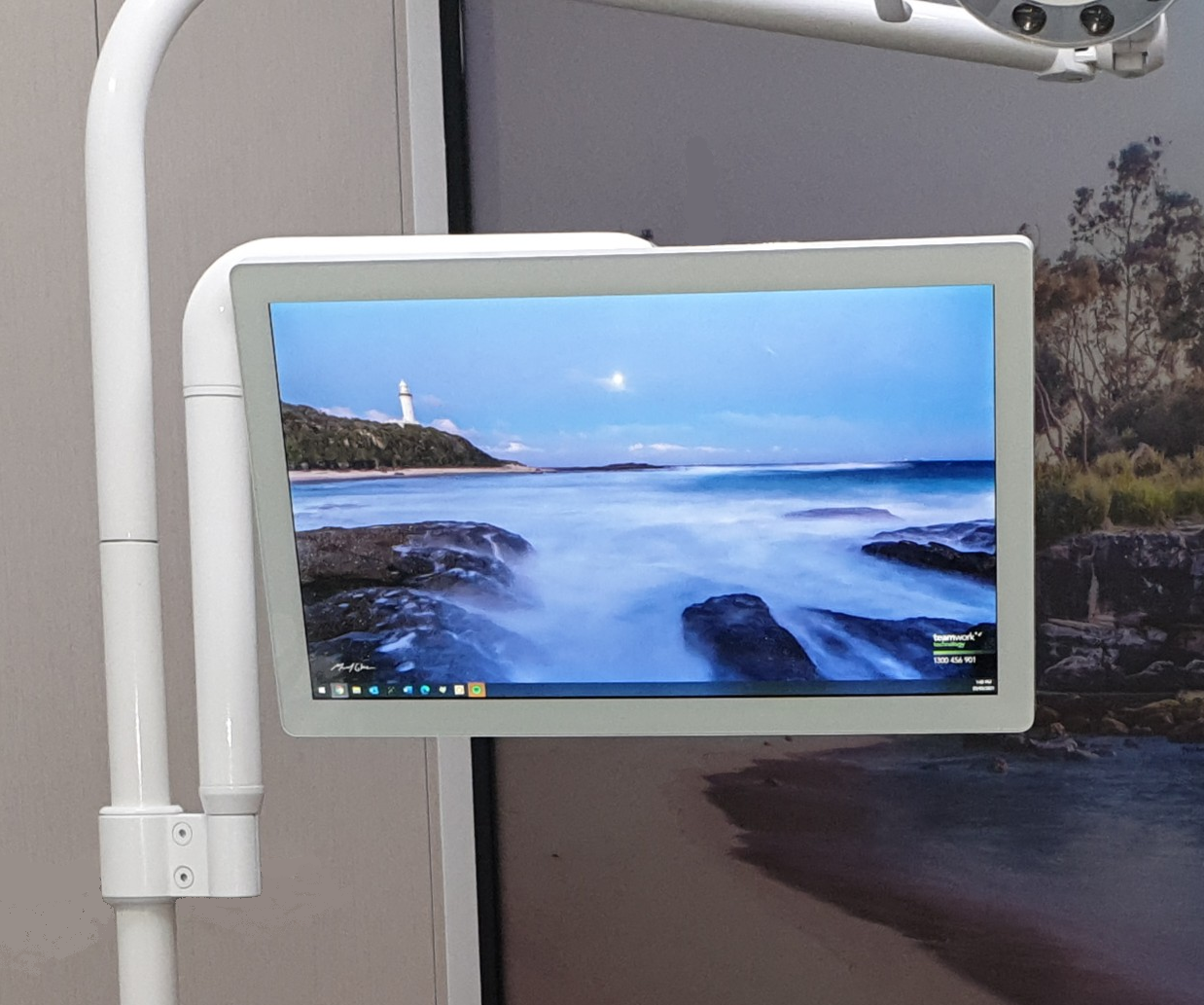 A mounted monitor displaying a coastal scene in a dentist's office; white arm, beach wallpaper.