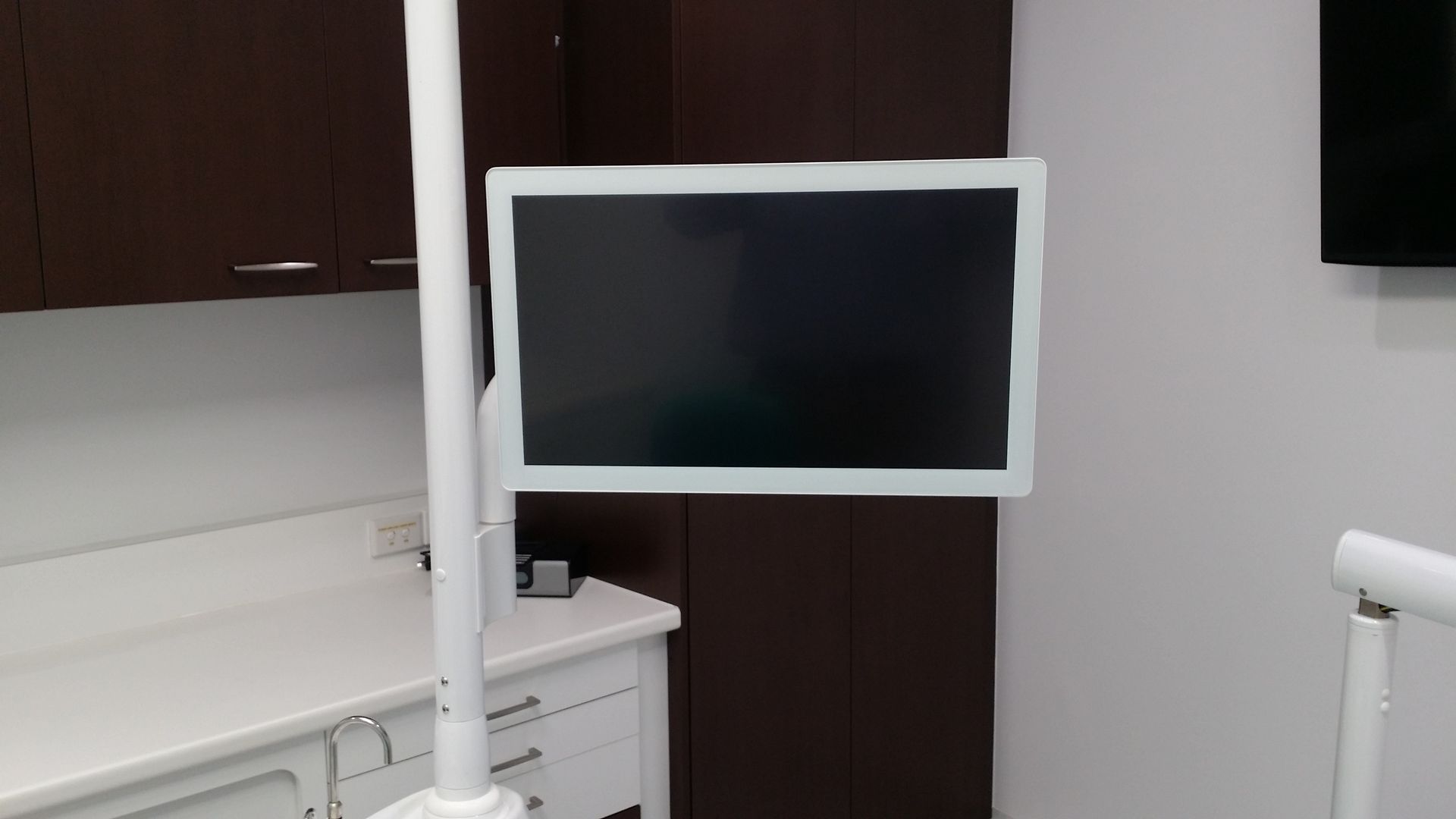 A dental office with a white monitor mounted on a pole, and white cabinetry.